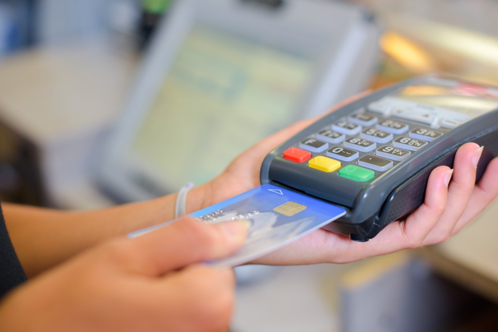 A person holding a credit card and swiping it through a machine